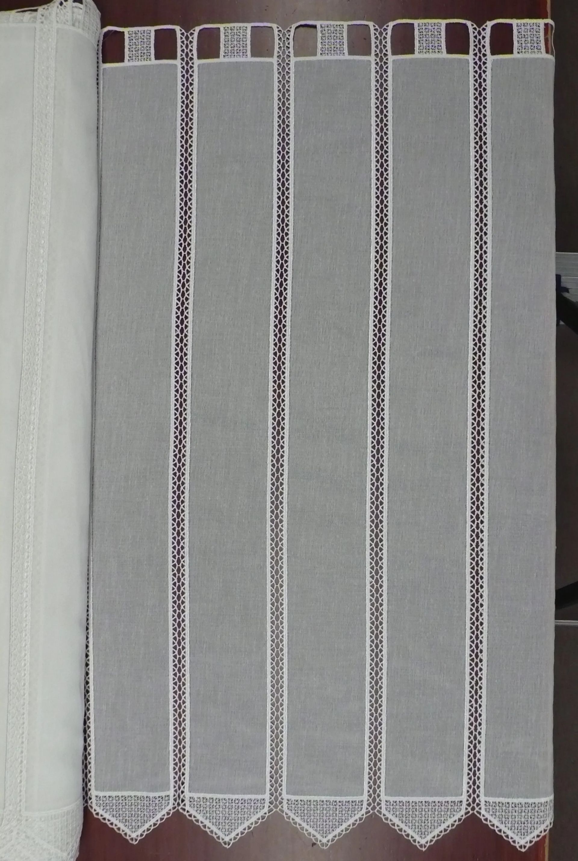 Una cortina blanca con ribete de encaje reposa sobre una mesa de madera.