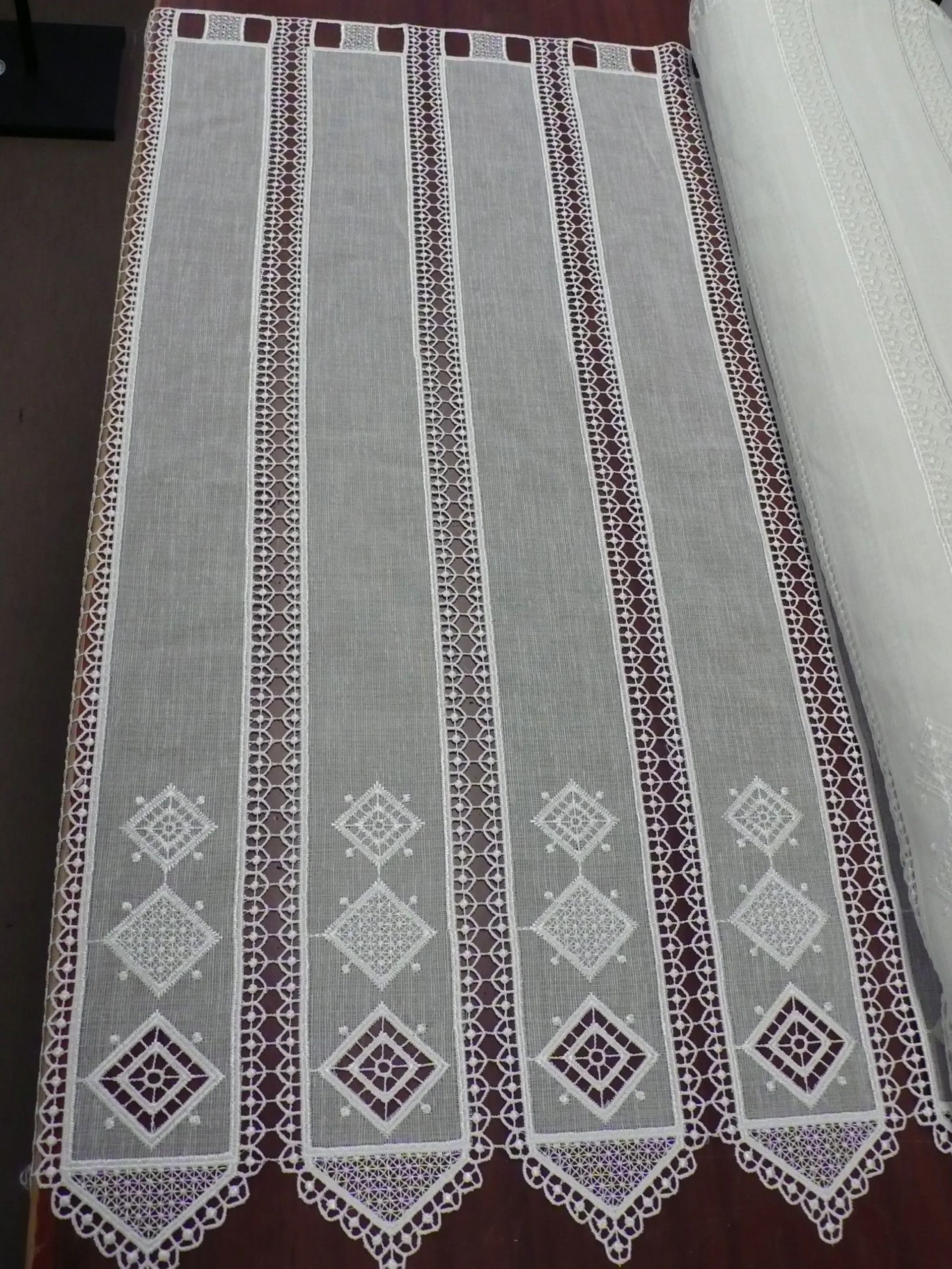 Una cortina de encaje blanco con un borde marrón reposa sobre una mesa.