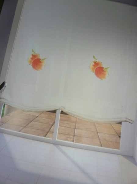 Una cortina blanca con dos flores naranjas cuelga de una ventana.