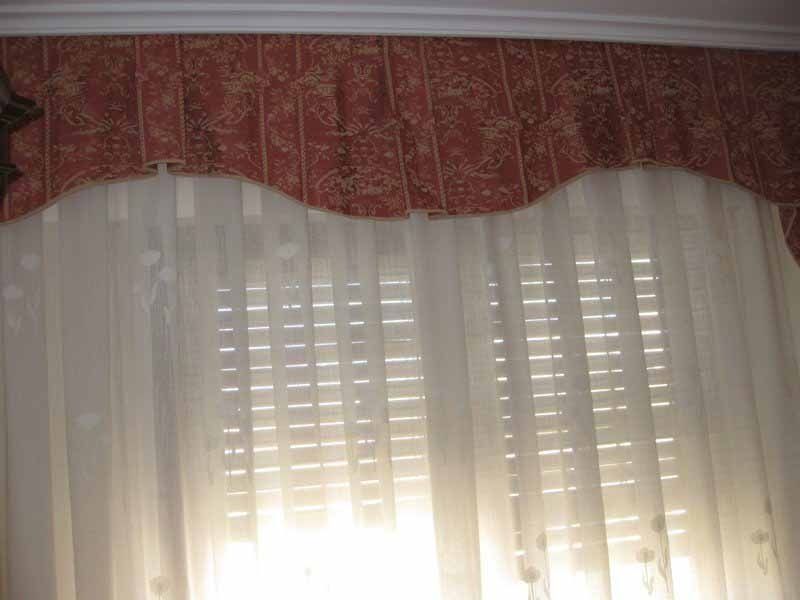 Un primer plano de una ventana con una cenefa roja y cortinas blancas.