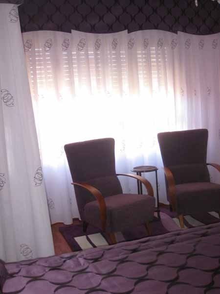 Dos sillas frente a una ventana con cortinas blancas.