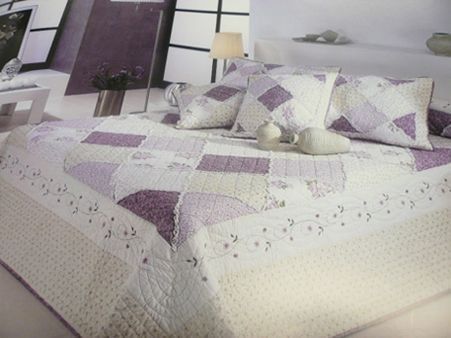 Una cama con una colcha y almohadas moradas y blancas.
