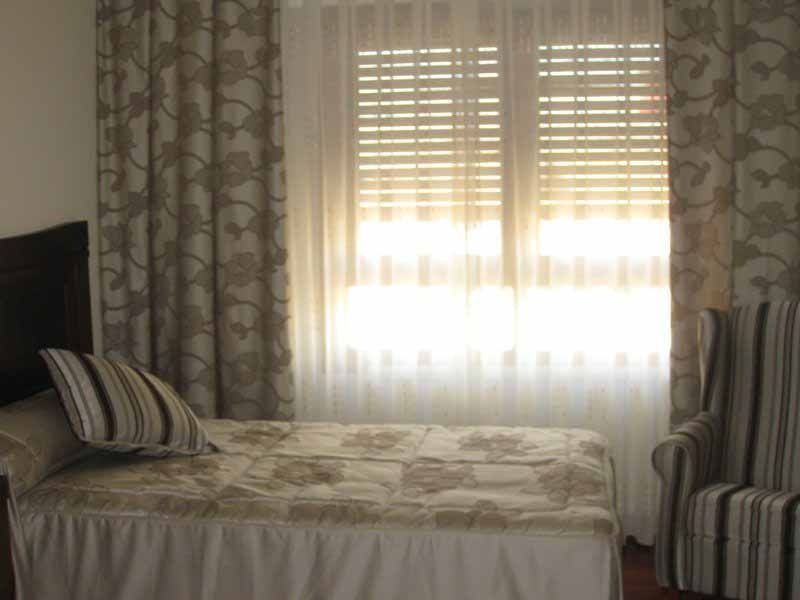 Un dormitorio con una cama, una silla y una ventana.