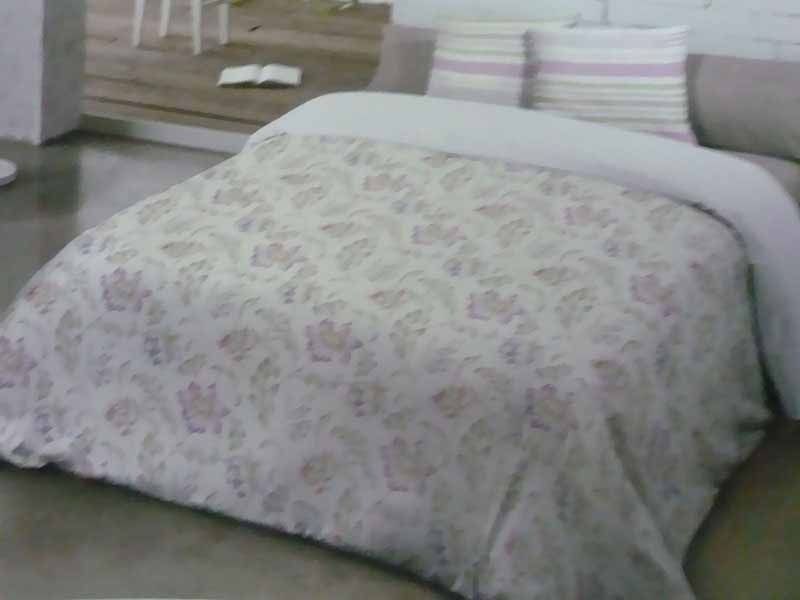 Una cama con un edredón floral y almohadas encima.