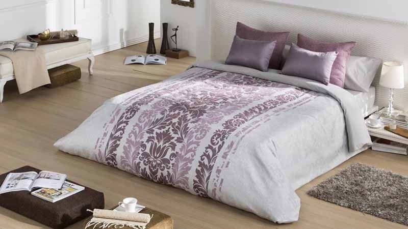 Una cama con un edredón morado y almohadas en un dormitorio.