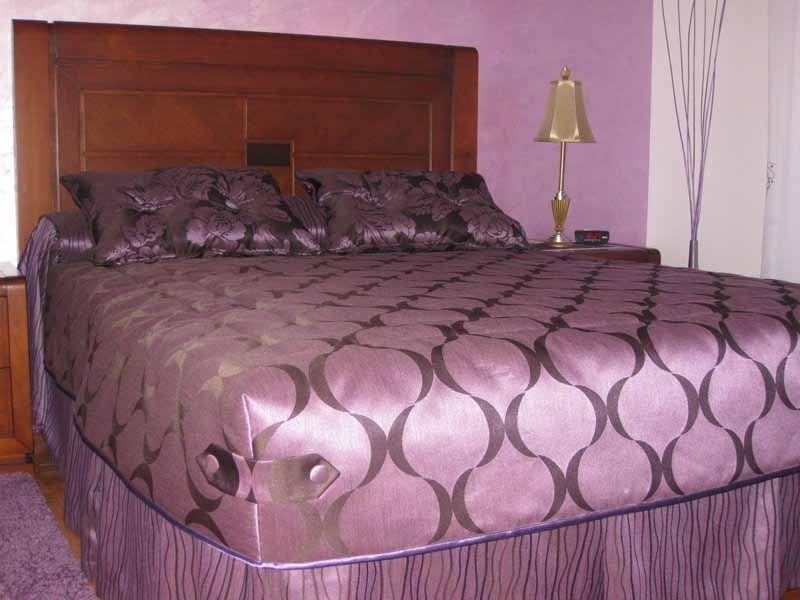 Una cama con un edredón morado y almohadas en un dormitorio.