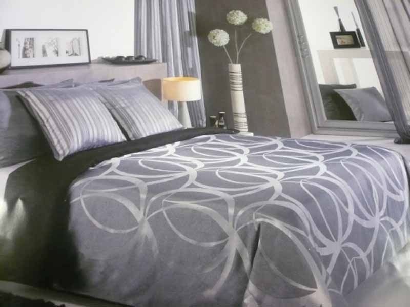 Una cama con un edredón gris y almohadas en un dormitorio.