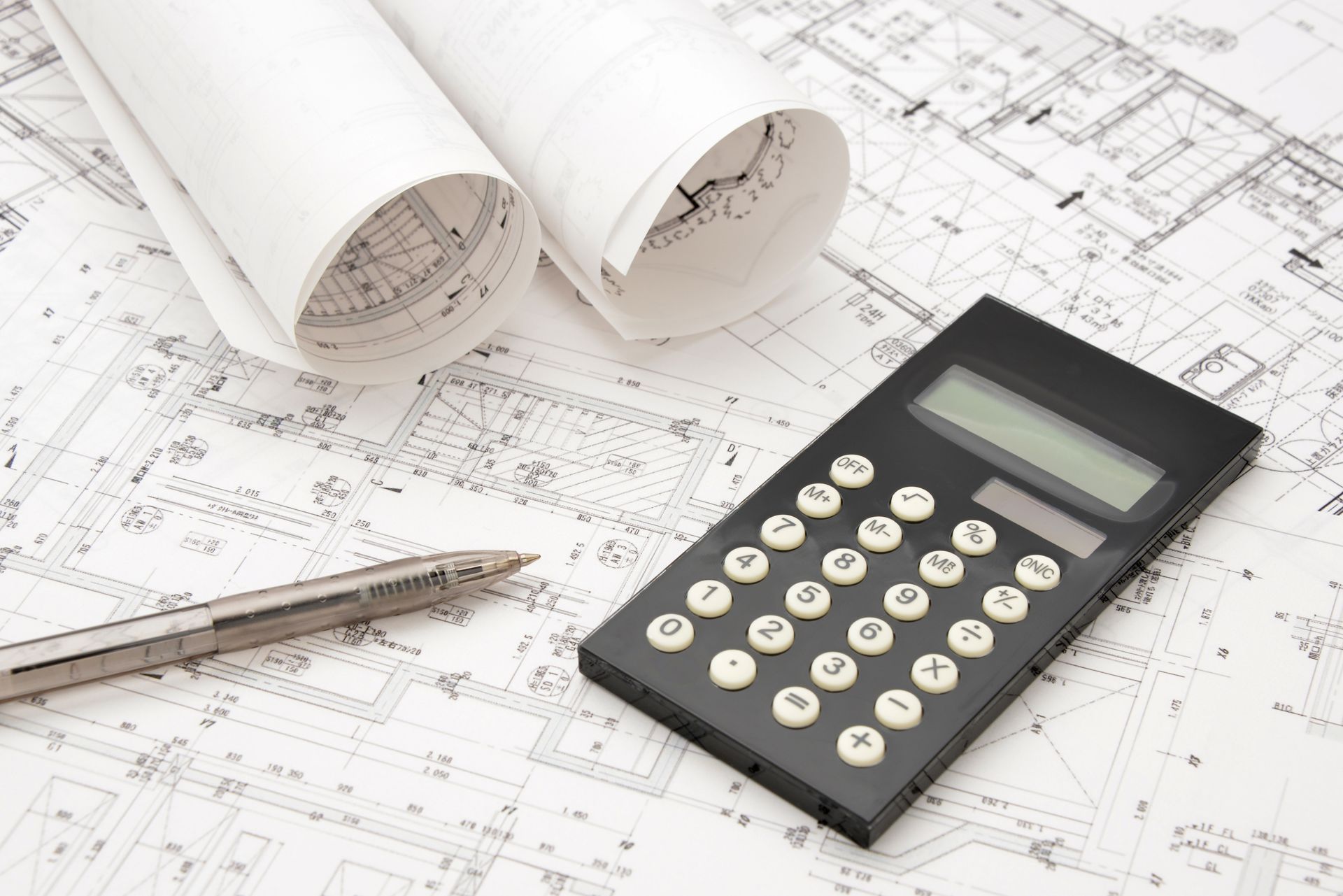 Une calculatrice et un crayon posés sur les plans d'une maison.