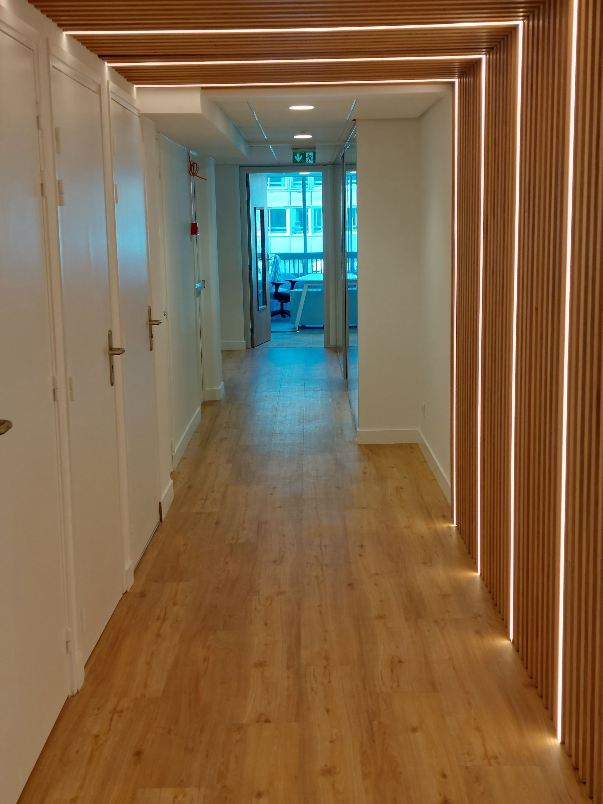 Couloir avec lambris et portes en bois, éclairé par des spots encastrés et un cadre en bois.