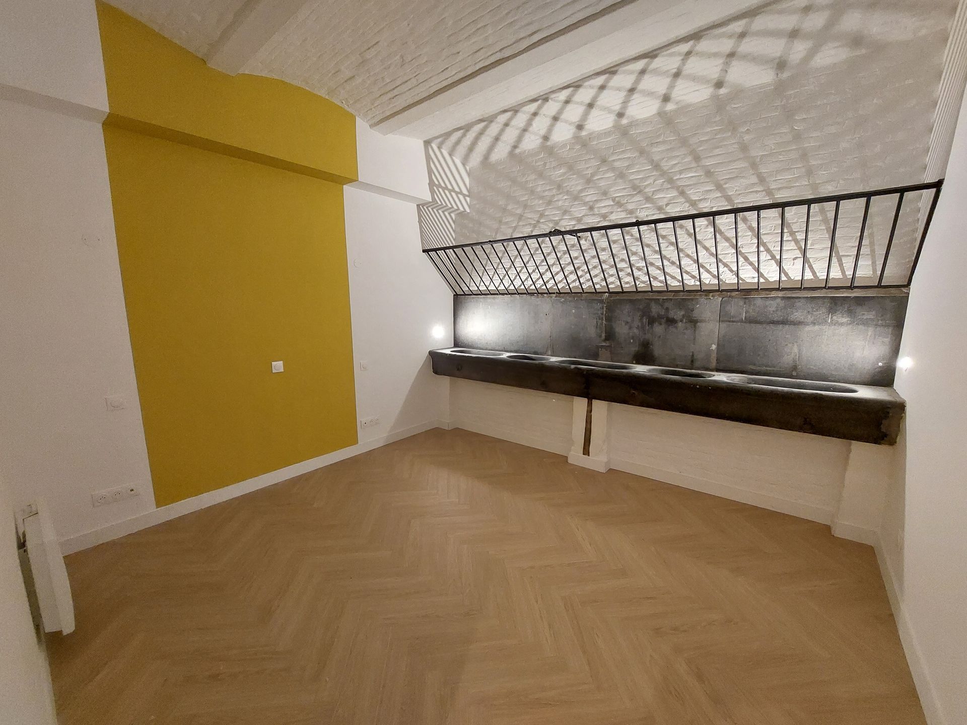 Pièce vide avec un mur d'accent jaune, un parquet et des éléments décoratifs en métal au-dessus d'un comptoir sombre.