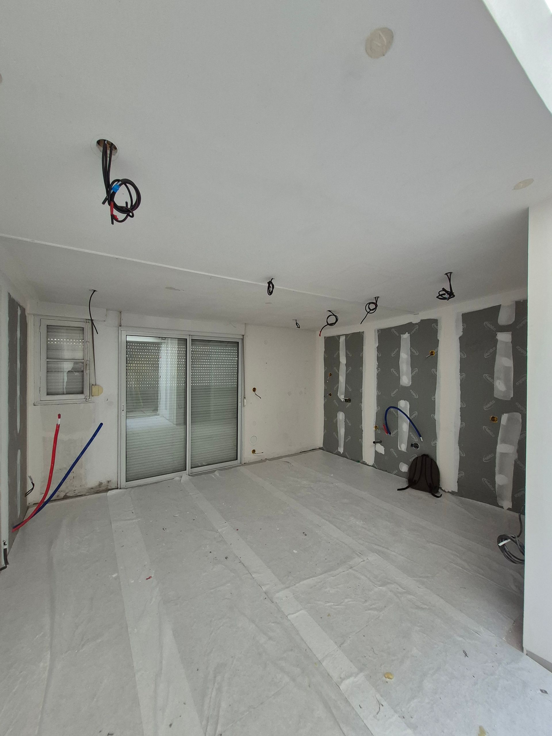 Pièce intérieure en construction avec câblage apparent, cloisons sèches et porte coulissante en verre.