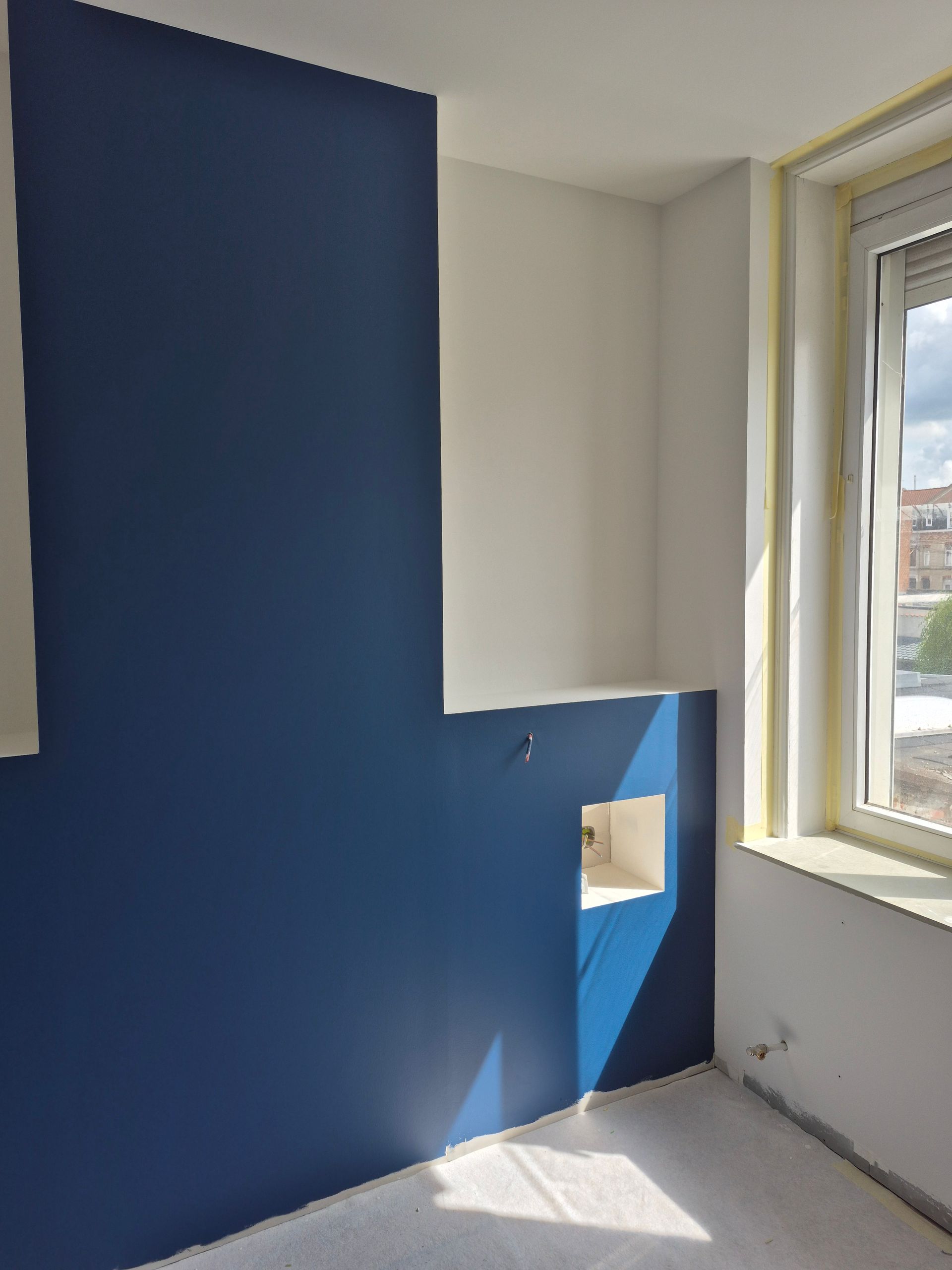 Intérieur de la pièce : mur d’accent bleu, murs blancs, fenêtre laissant entrer la lumière du soleil.