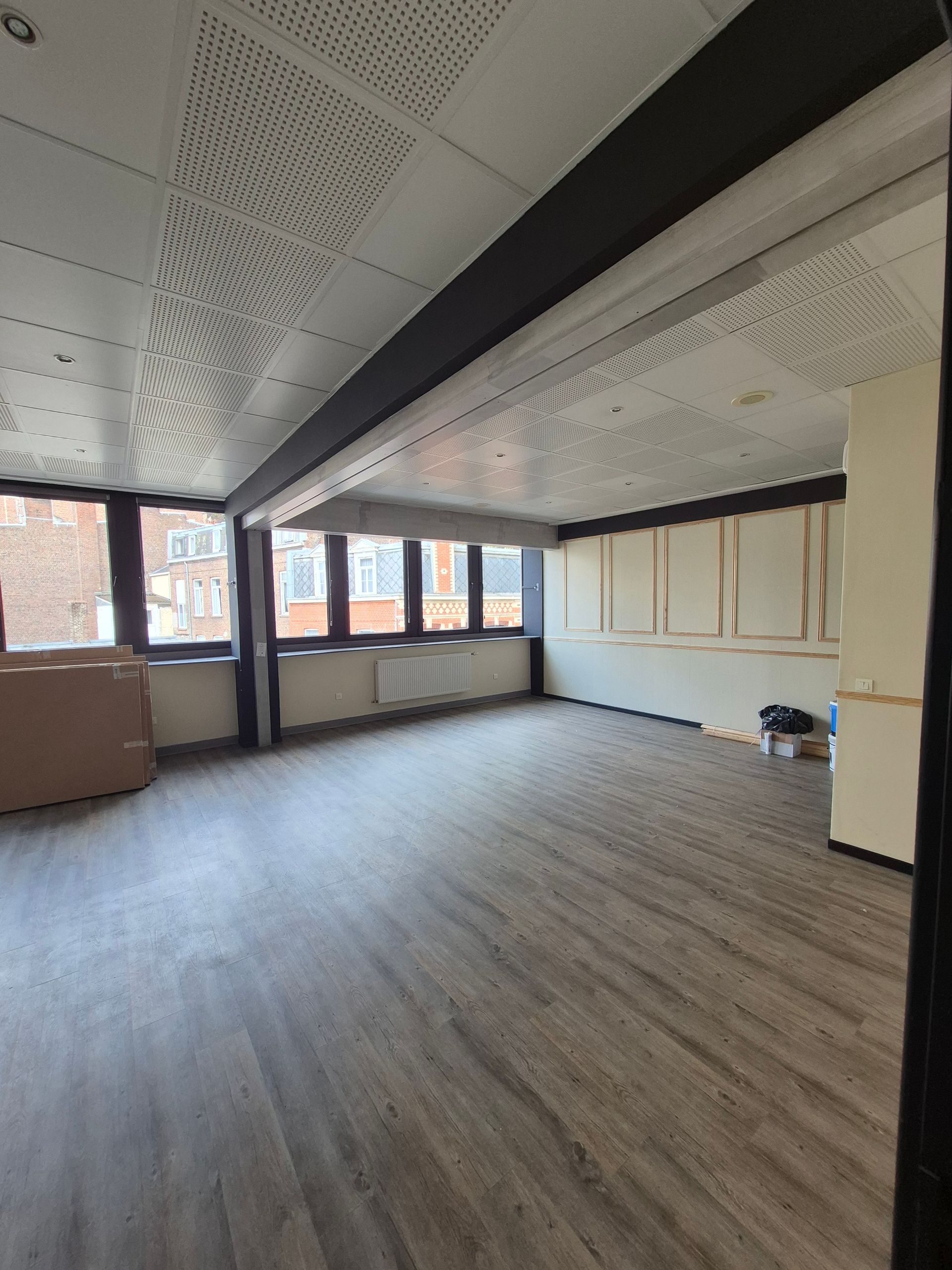 Espace de bureau vide avec fenêtres, sol gris et panneaux de plafond blancs.