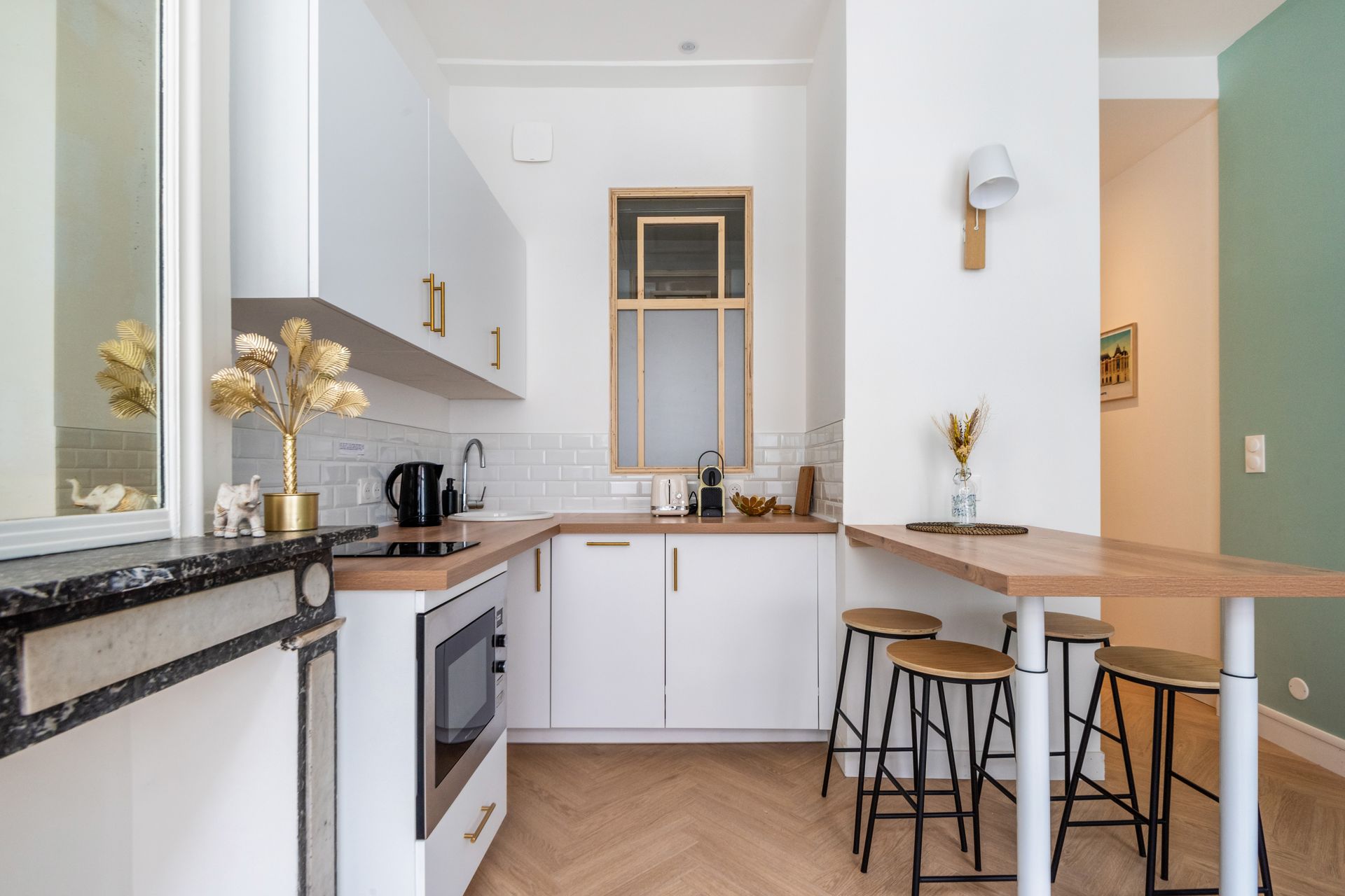 Petite cuisine avec placards blancs, plans de travail en bois et un coin repas avec tabourets.