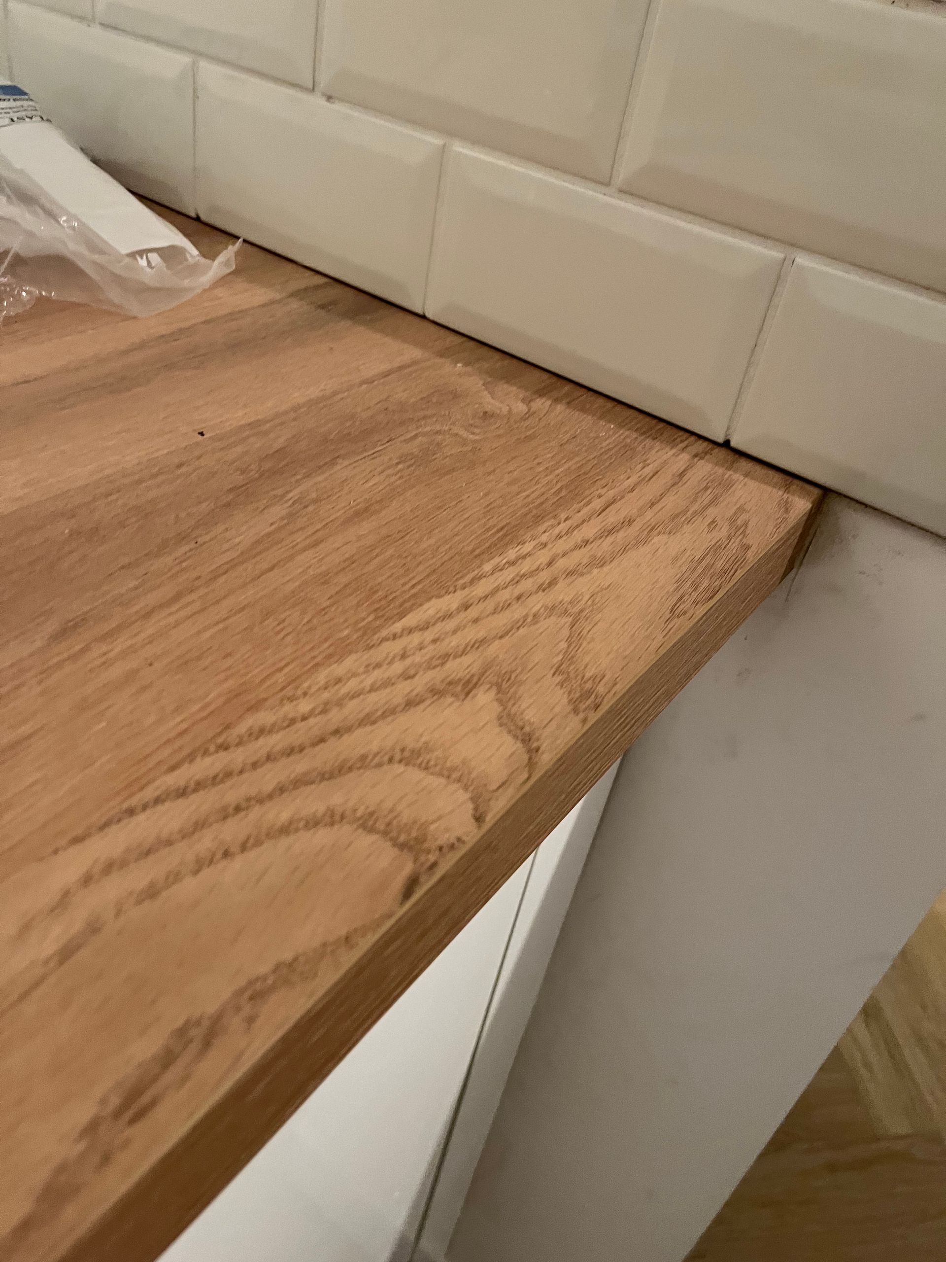 Gros plan d'un plan de travail en bois devant une crédence carrelée blanche et un meuble blanc.