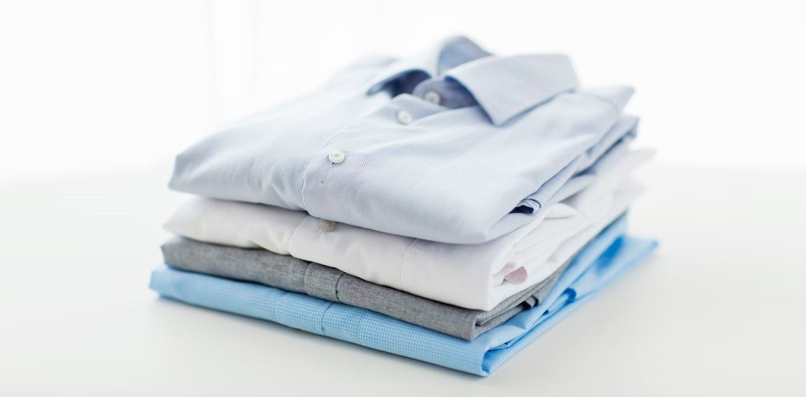 Una pila de camisas y suéteres doblados sobre una superficie blanca.