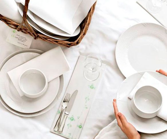 Una persona está poniendo una mesa con platos y tazas blancos.