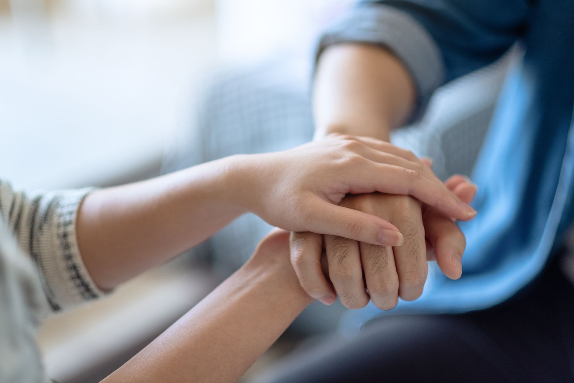 Eine Hand hält sanft die Hand einer anderen und bietet so Halt. Innenaufnahme, sanftes Licht.