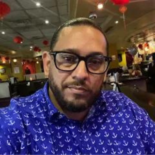 A man wearing glasses and a blue shirt with anchors on it is taking a selfie in a restaurant.