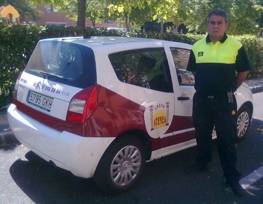 Un hombre con un chaleco amarillo se encuentra frente a un automóvil rojo y blanco.