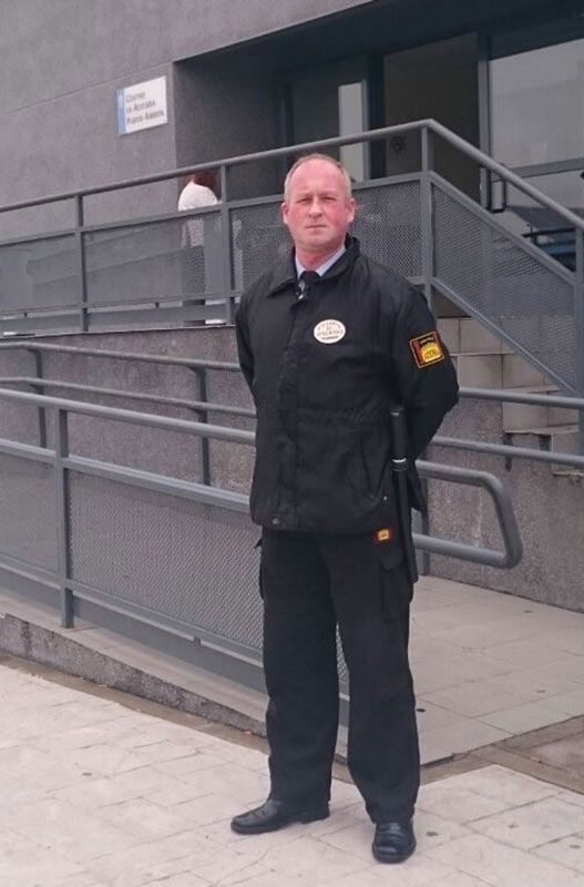 Un hombre con uniforme negro está parado frente a un edificio.