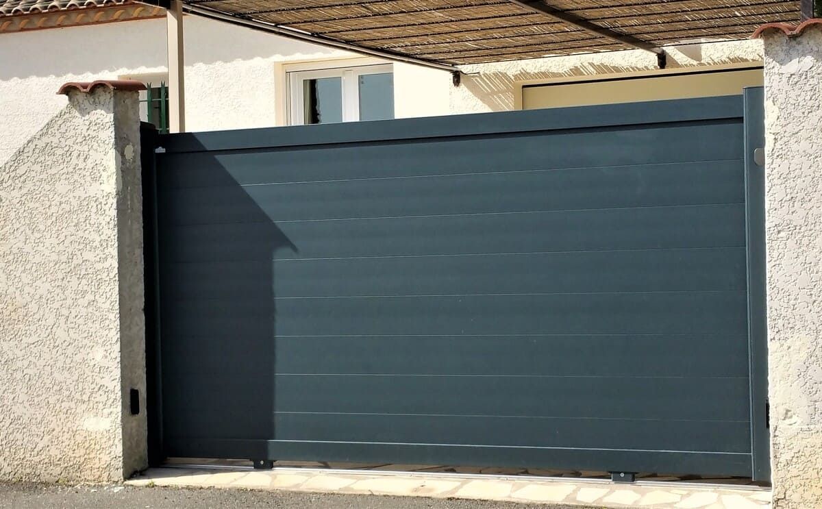 Portail coulissant gris sur une propriété résidentielle, entre des piliers en stuc.