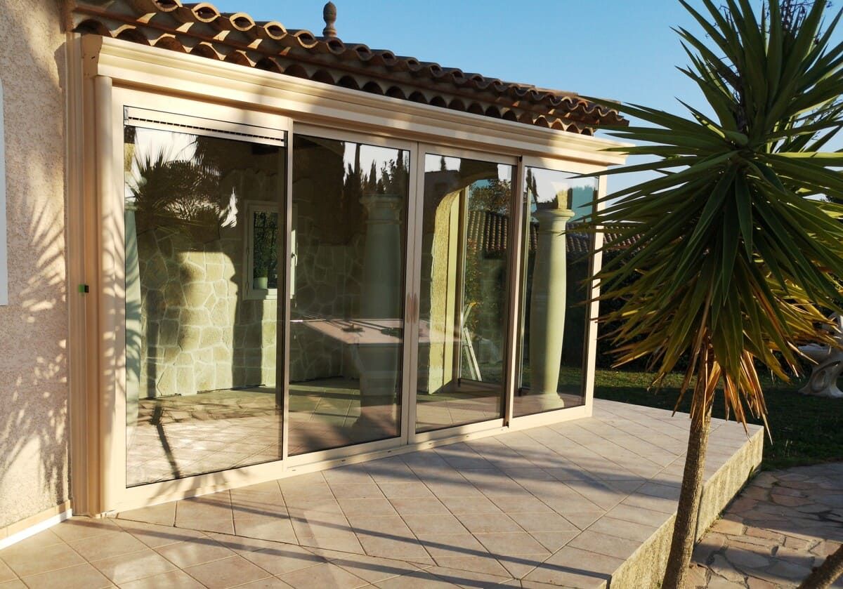 Patio ensoleillé avec de grandes portes vitrées reflétant les colonnes intérieures.