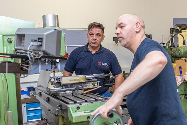 Zwei Männer arbeiten in einer Fabrik an einer Maschine.