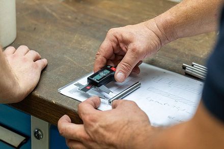 Ein Mann misst ein Stück Metall mit einem digitalen Messschieber.