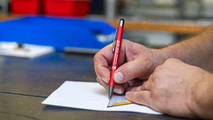 Eine Person schreibt mit einem Stift auf ein Blatt Papier.