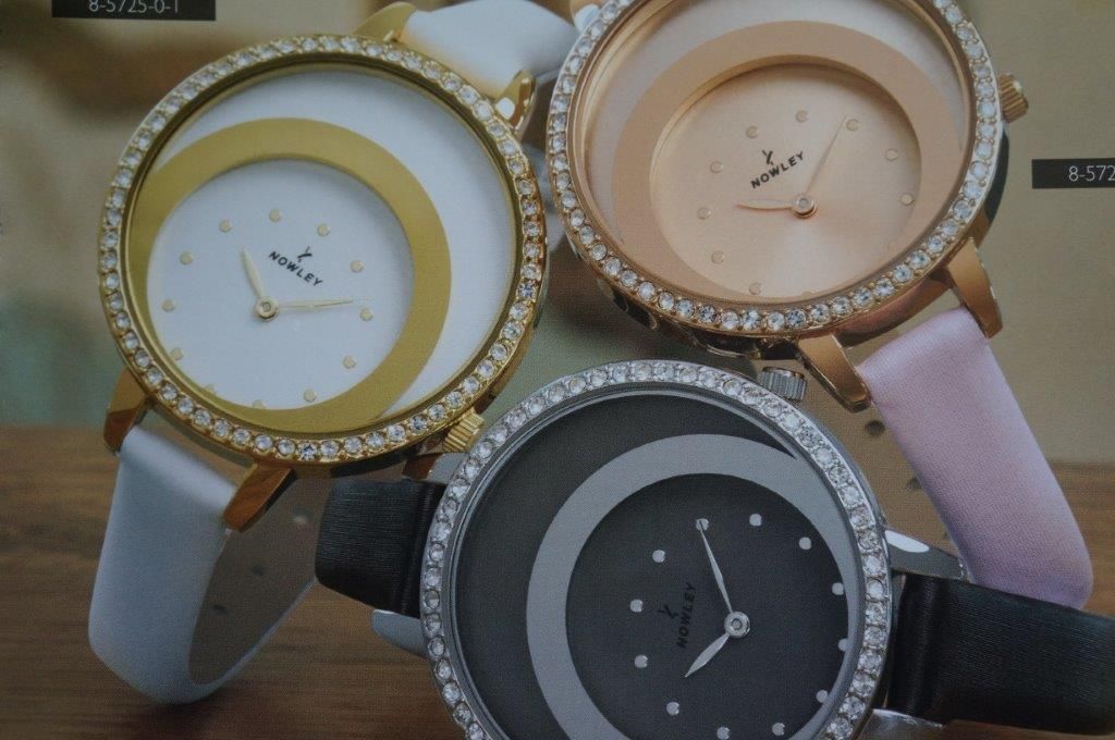 Tres relojes de mujer se exhiben sobre una mesa de madera.