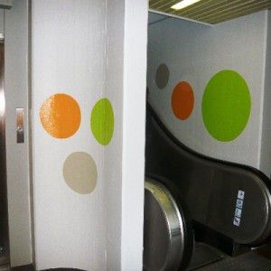 Eine Rolltreppe mit auf die Wand neben einem Aufzug gemalten Kreisen. Maler Lüscher GmbH