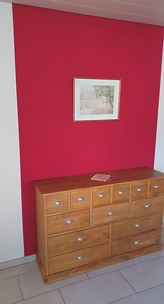 Vor einer roten Wand steht eine Holzkommode. Maler Lüscher GmbH