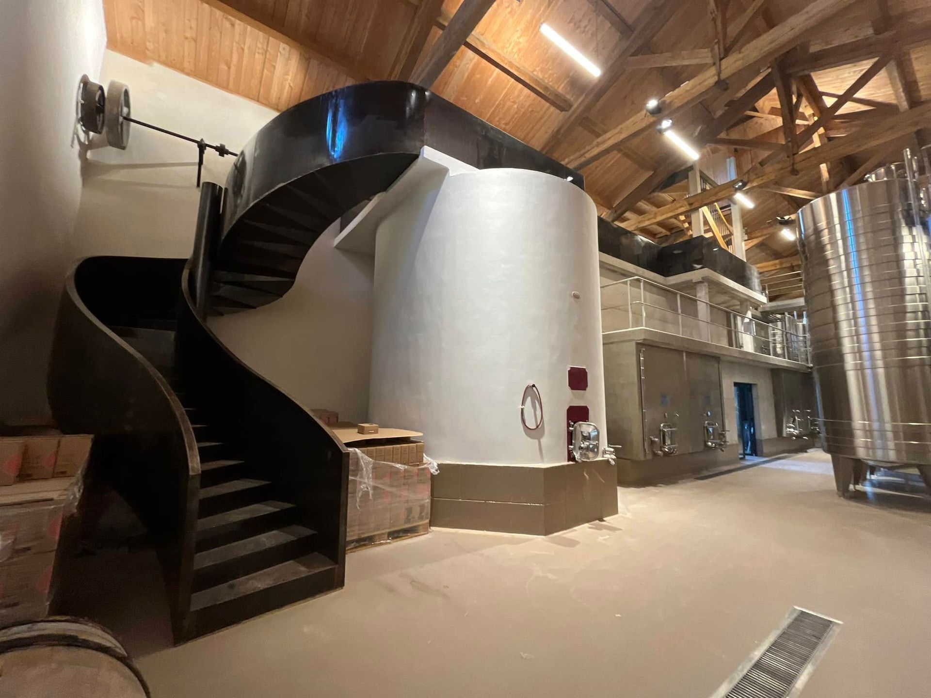 Une installation industrielle moderne avec un escalier en colimaçon noir, une grande cuve cylindrique blanche et de hautes cuves de stockage en acier.