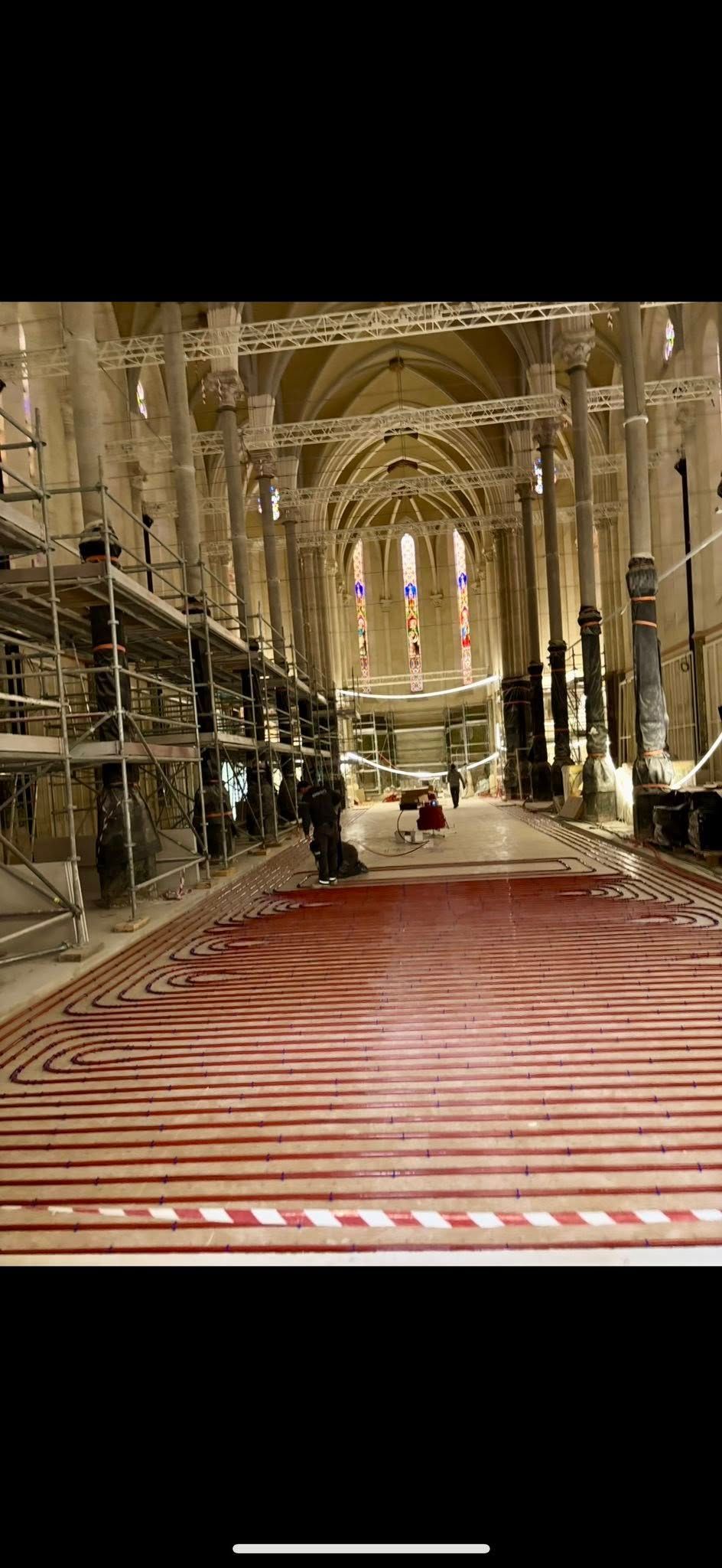 L'intérieur d'une église en rénovation, avec ses colonnes imposantes, ses échafaudages et son sol rouge texturé.