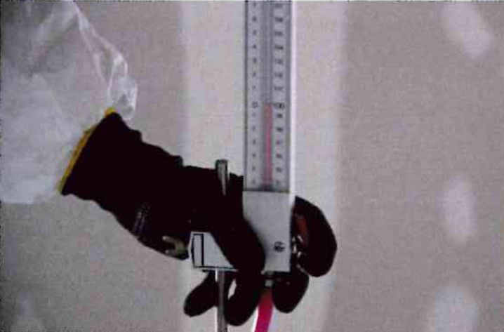 Une personne en tenue de protection tient un instrument scientifique vertical avec une colonne de fluide rose vif.