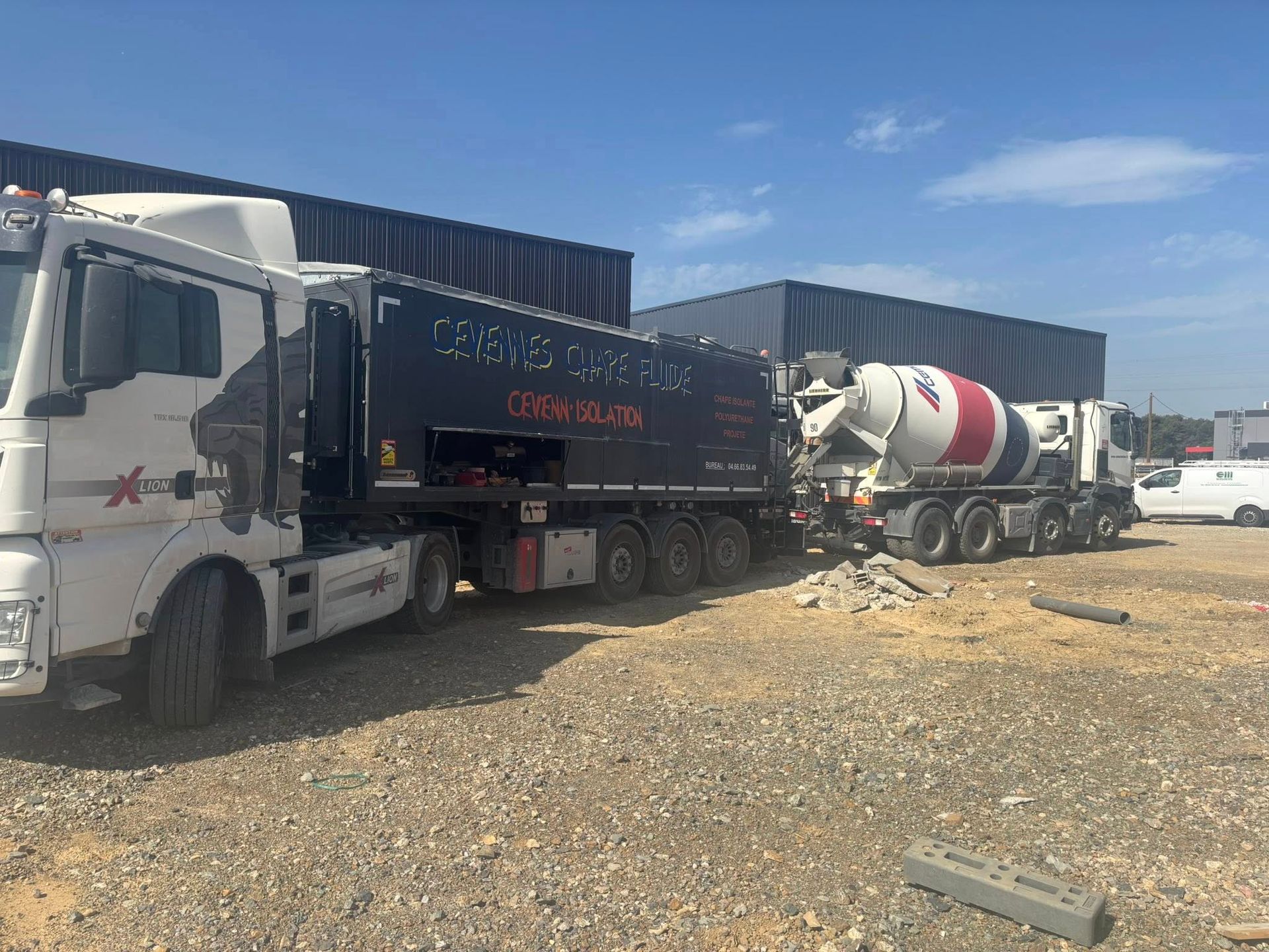 Un semi-remorque blanc garé à côté d'un camion malaxeur à béton rouge, blanc et gris sur un terrain gravillonné sous un ciel bleu.