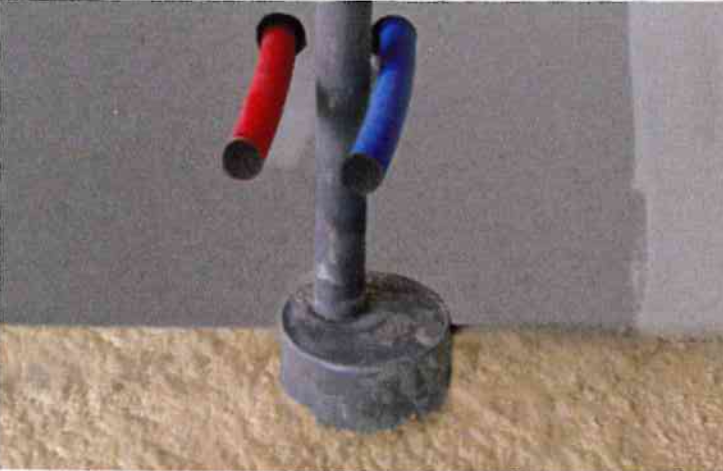 Un tuyau vertical gris repose sur une surface texturée, avec un petit tuyau à manchon rouge à gauche et un autre à manchon bleu.