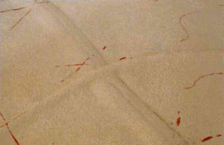 Surface beige texturée présentant une légère couture en forme de X en relief et plusieurs marques rouges irrégulières et éparses.