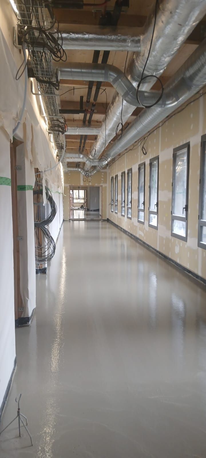 Un long et étroit couloir intérieur en construction, avec des murs nus, des conduits d'aération argentés apparents et un sol lisse et clair.