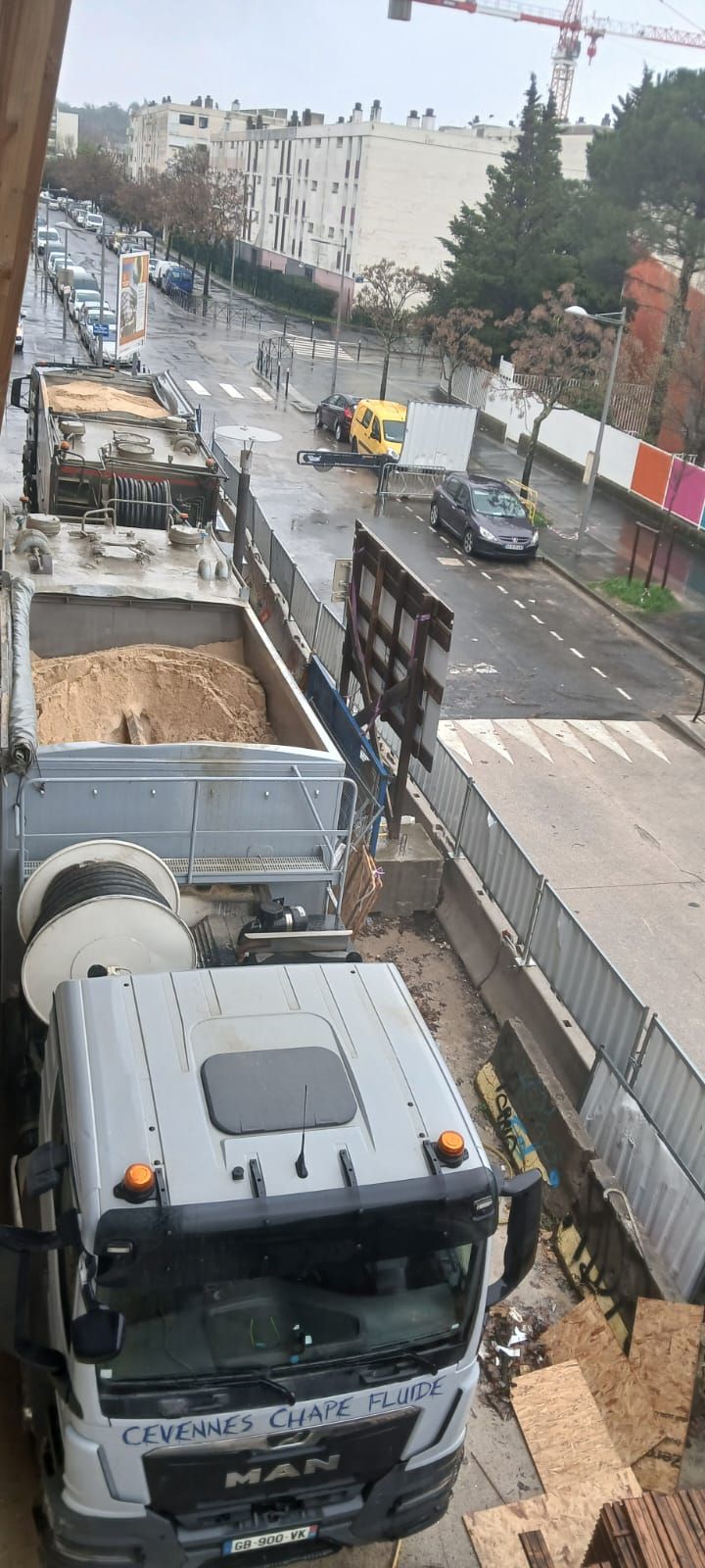 Vue en plongée d'un camion-benne blanc chargé de terre, stationné dans une rue de la ville à côté d'un chantier de construction clôturé.
