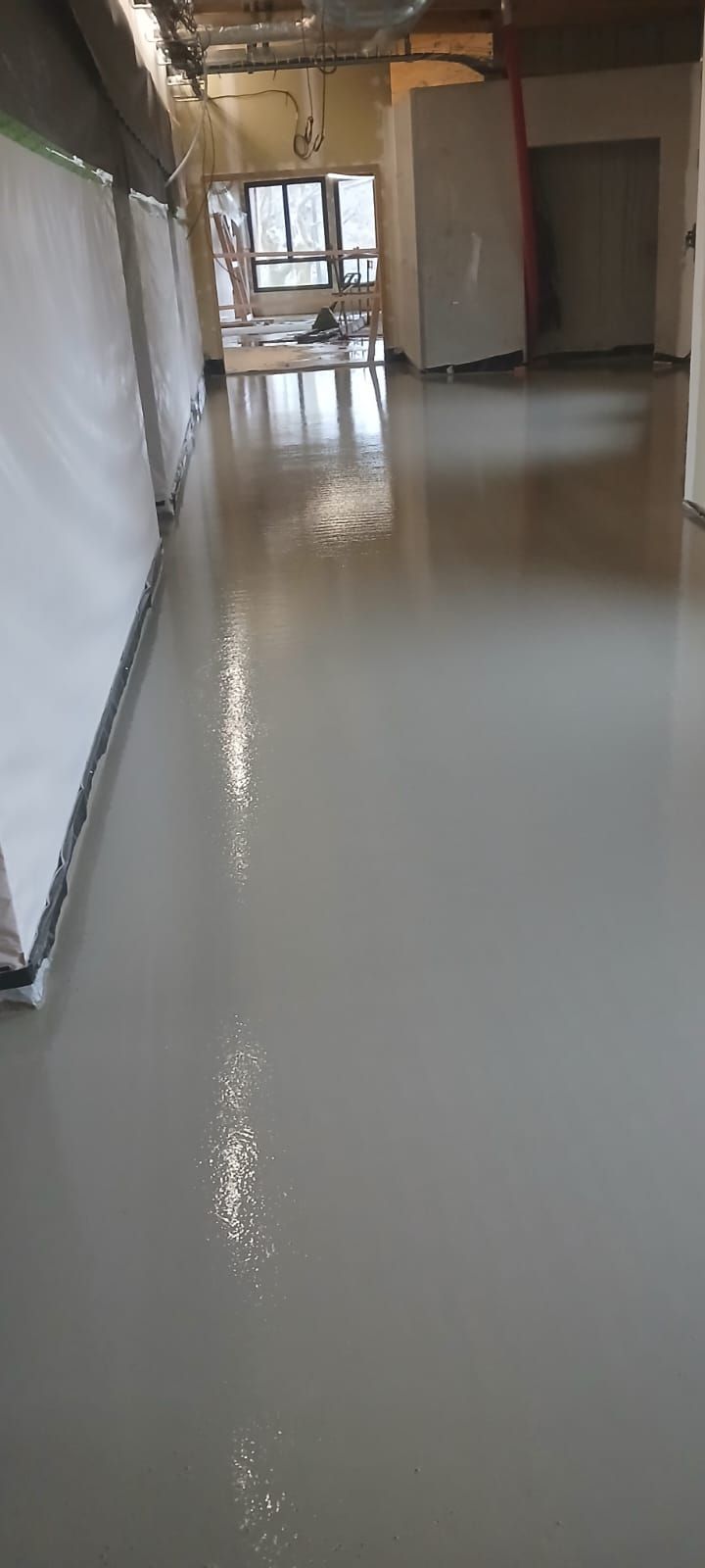 Un couloir en construction, avec un sol en époxy gris clair lisse et brillant et des bâches de protection blanches sur les murs.