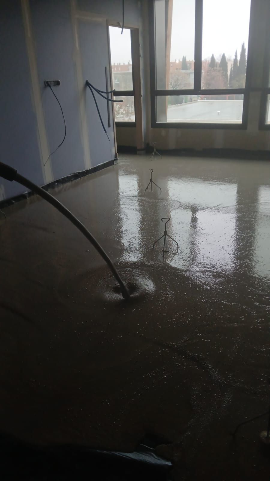 Lors d'un chantier de construction, un tuyau d'arrosage déverse du béton liquide sur le sol d'une pièce.