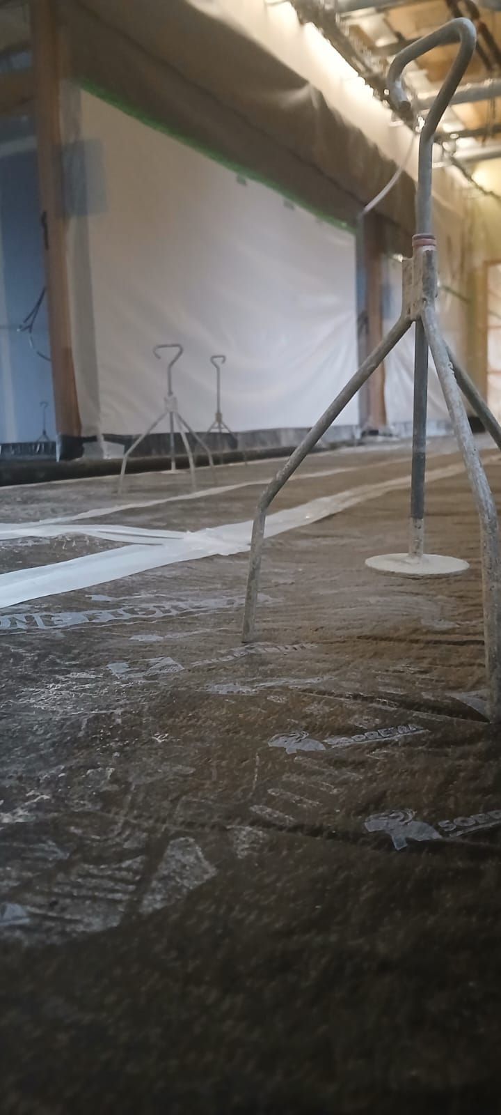 Un sol de chantier recouvert de béton sombre, avec des repères topographiques de type trépied disposés le long de la pièce.