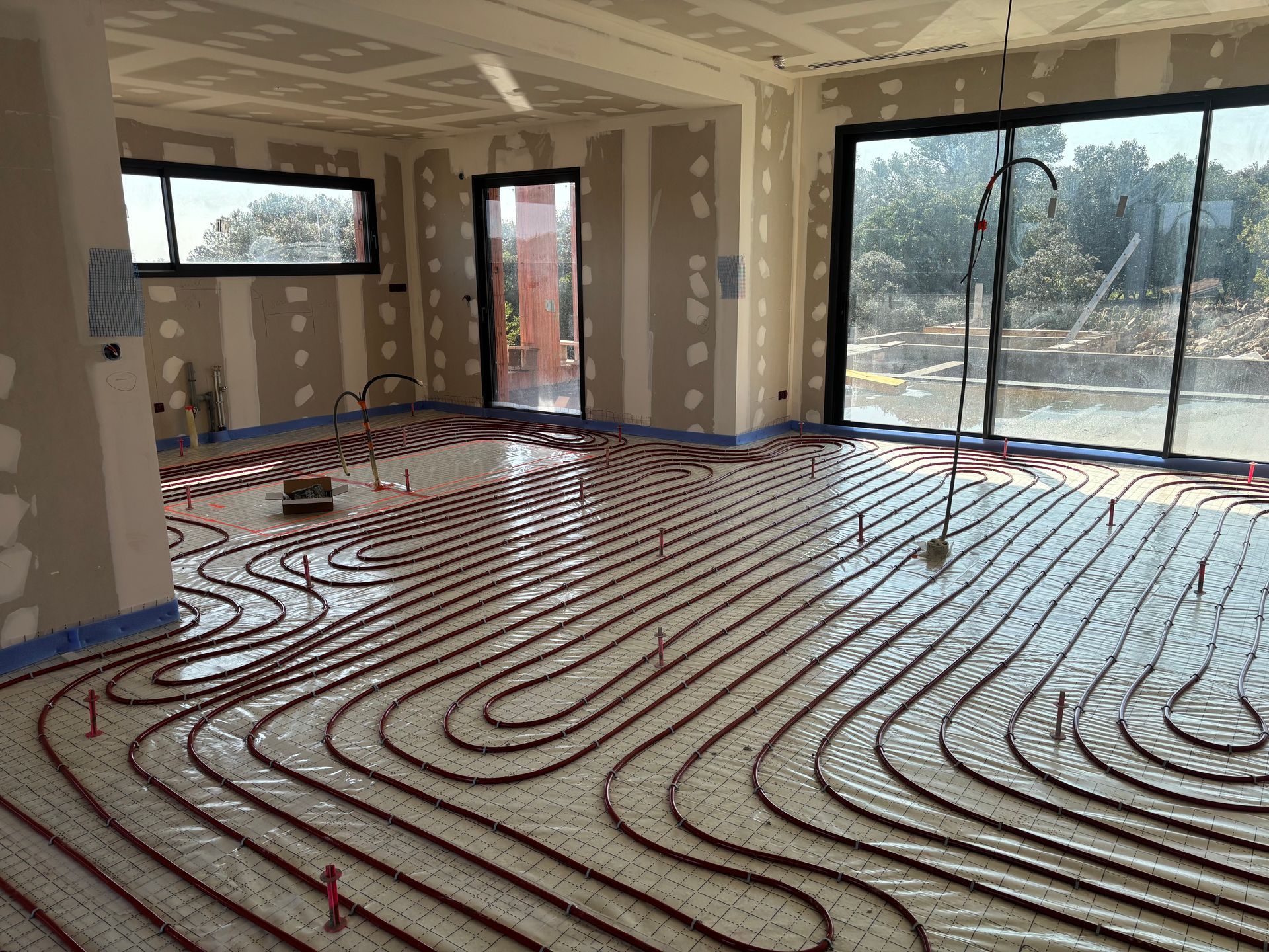 Intérieur d'une pièce en construction avec des tuyaux de chauffage au sol radiant rouges installés sur toute la surface.