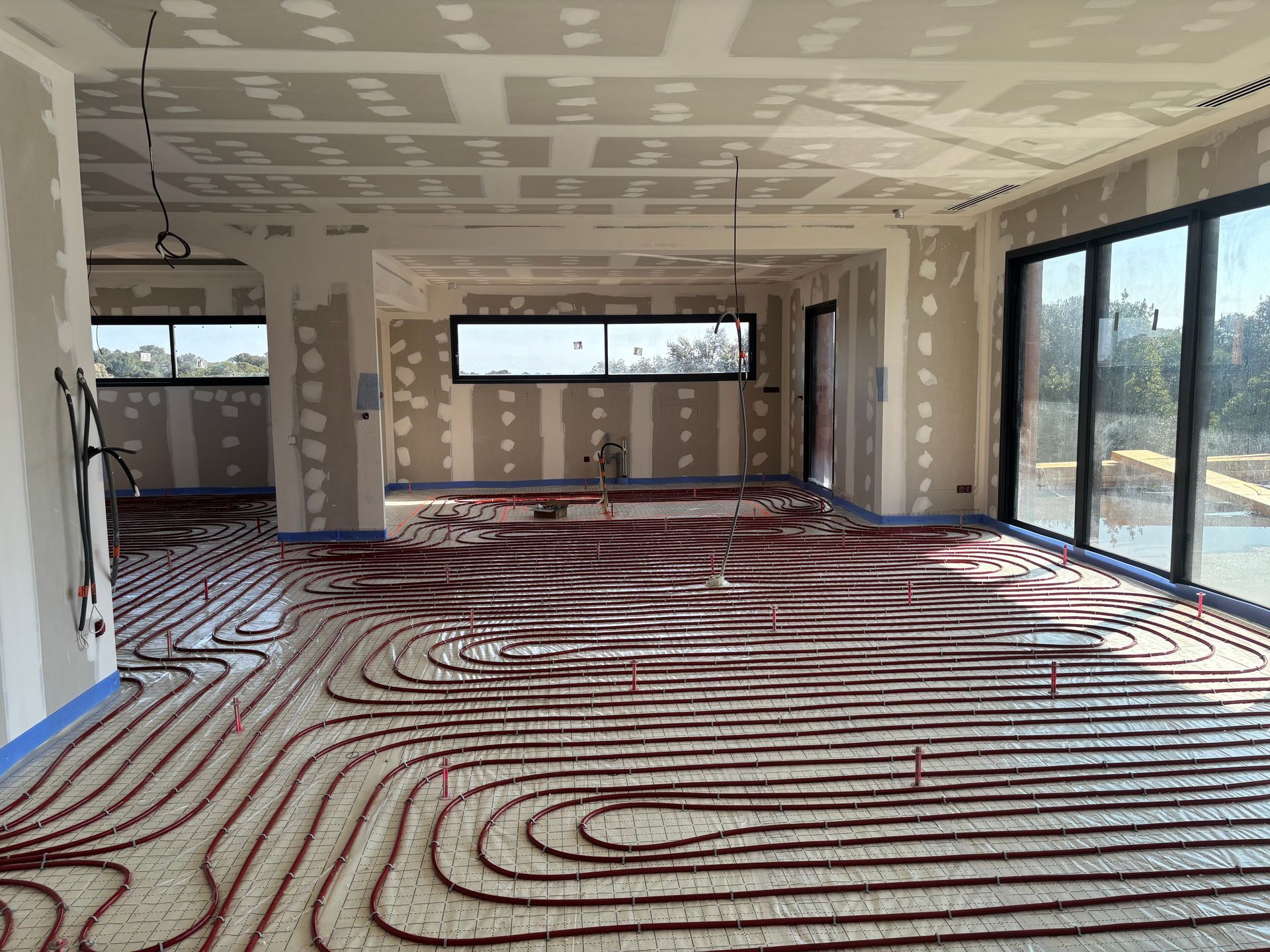 Des tuyaux de chauffage au sol radiant rouges sont installés en serpentin sur une chape en polyuréthane projeté et polyane quadrillé.