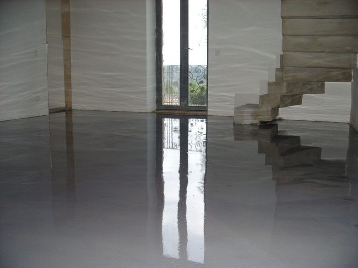 Une pièce moderne avec un sol gris lisse et brillant reflétant une haute fenêtre et un escalier en pierre.