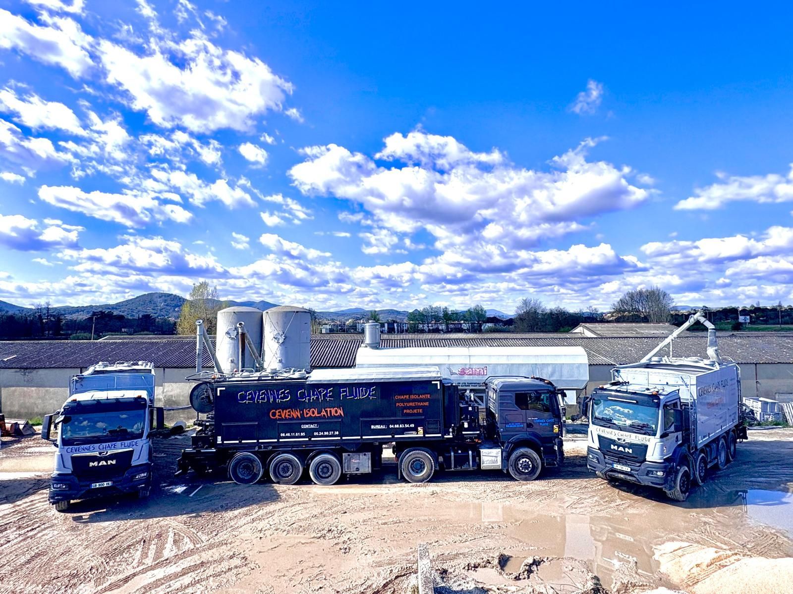 Trois camions stationnés sur un chantier boueux sous un ciel bleu nuageux.