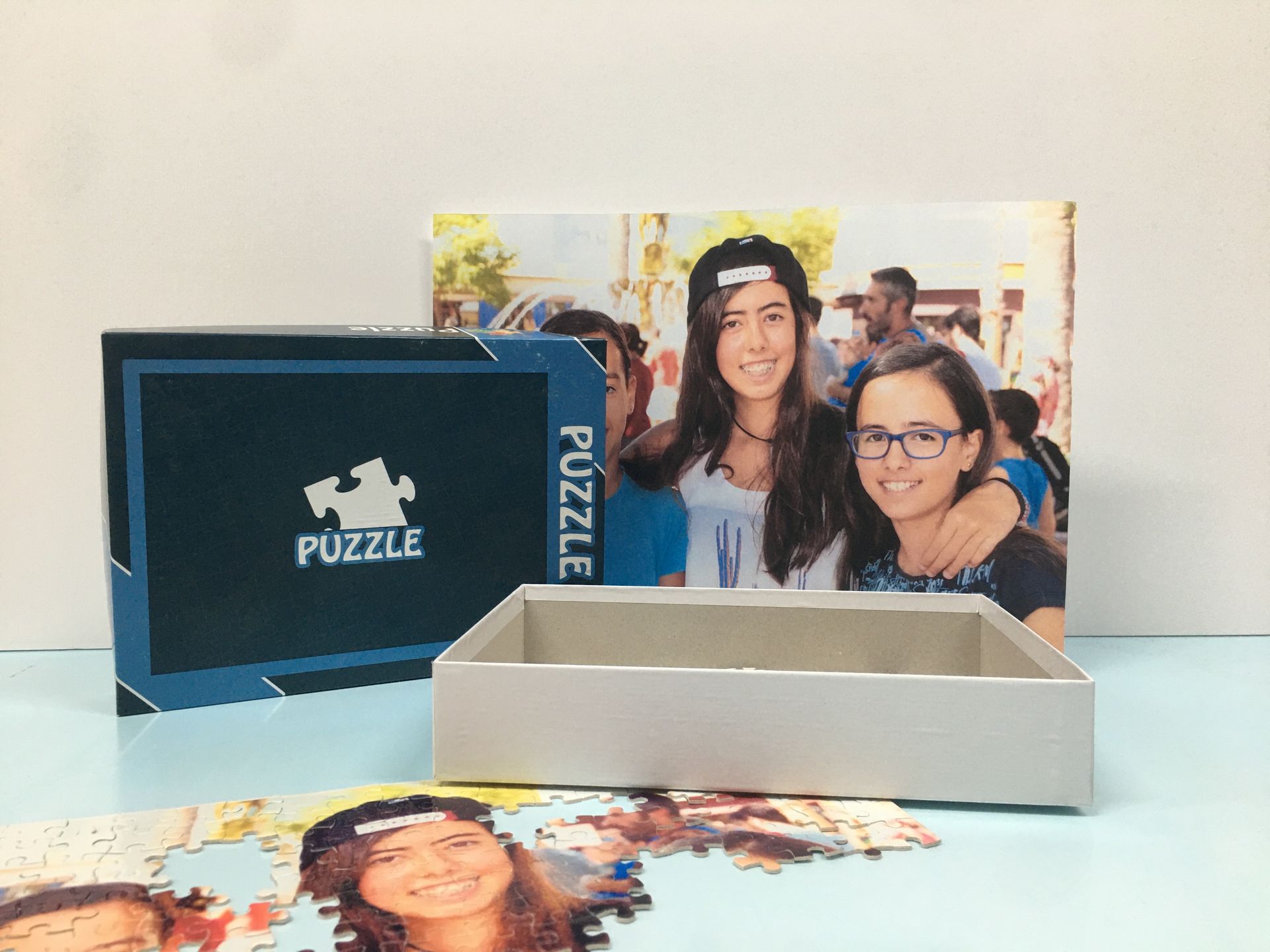 Caja de rompecabezas junto a un rompecabezas armado con dos personas sonrientes sobre una mesa.