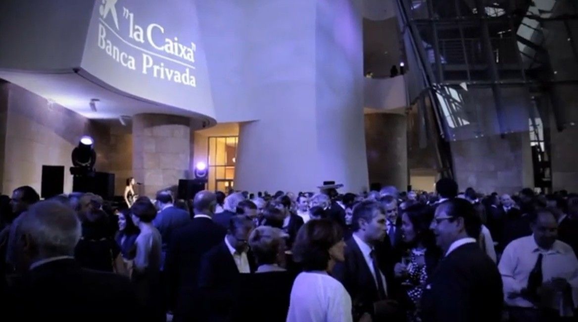 Una multitud se congregó frente al banco La Caixa por la noche bajo una iluminación azul.